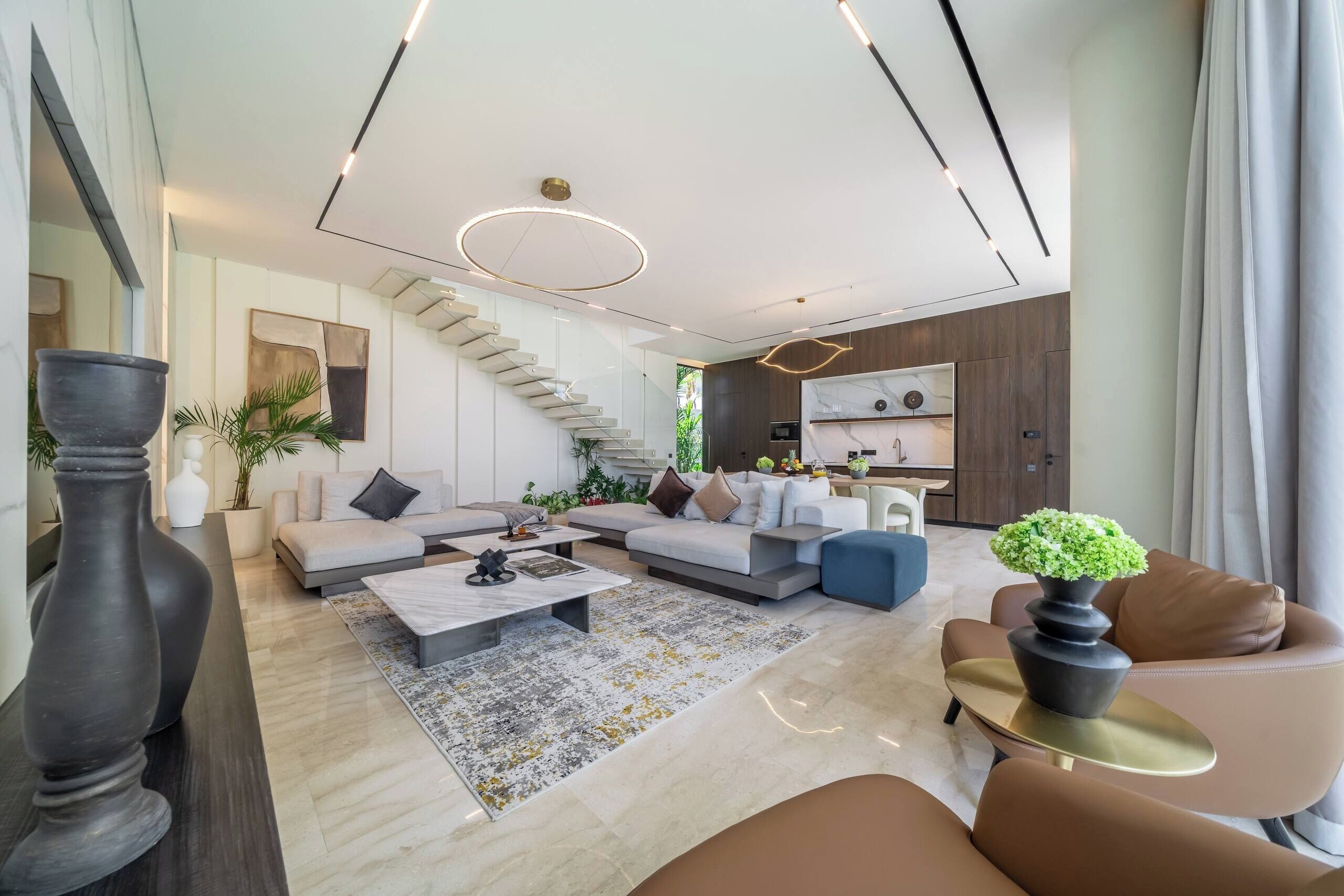 A modern living room with a staircase, a kitchen area, and a dining space.
