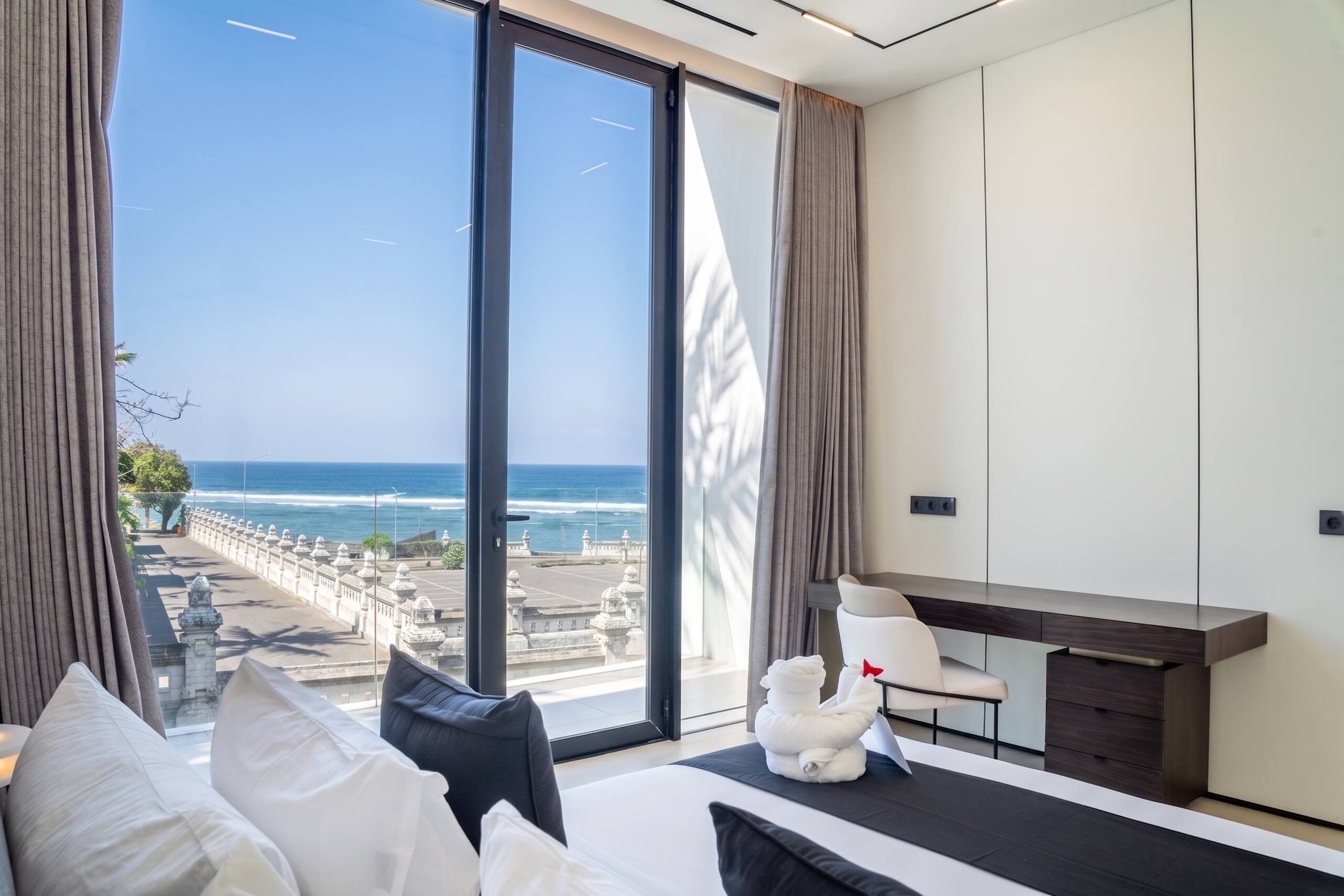 Ein modernes Hotelzimmer mit großem Fenster und Meerblick, einem Bett mit weißen Leinentüchern, einem Schreibtisch und einem Sessel.