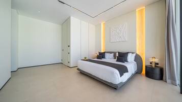 A modern bedroom with a large bed, a bedside table, a wall-mounted light, and a door.