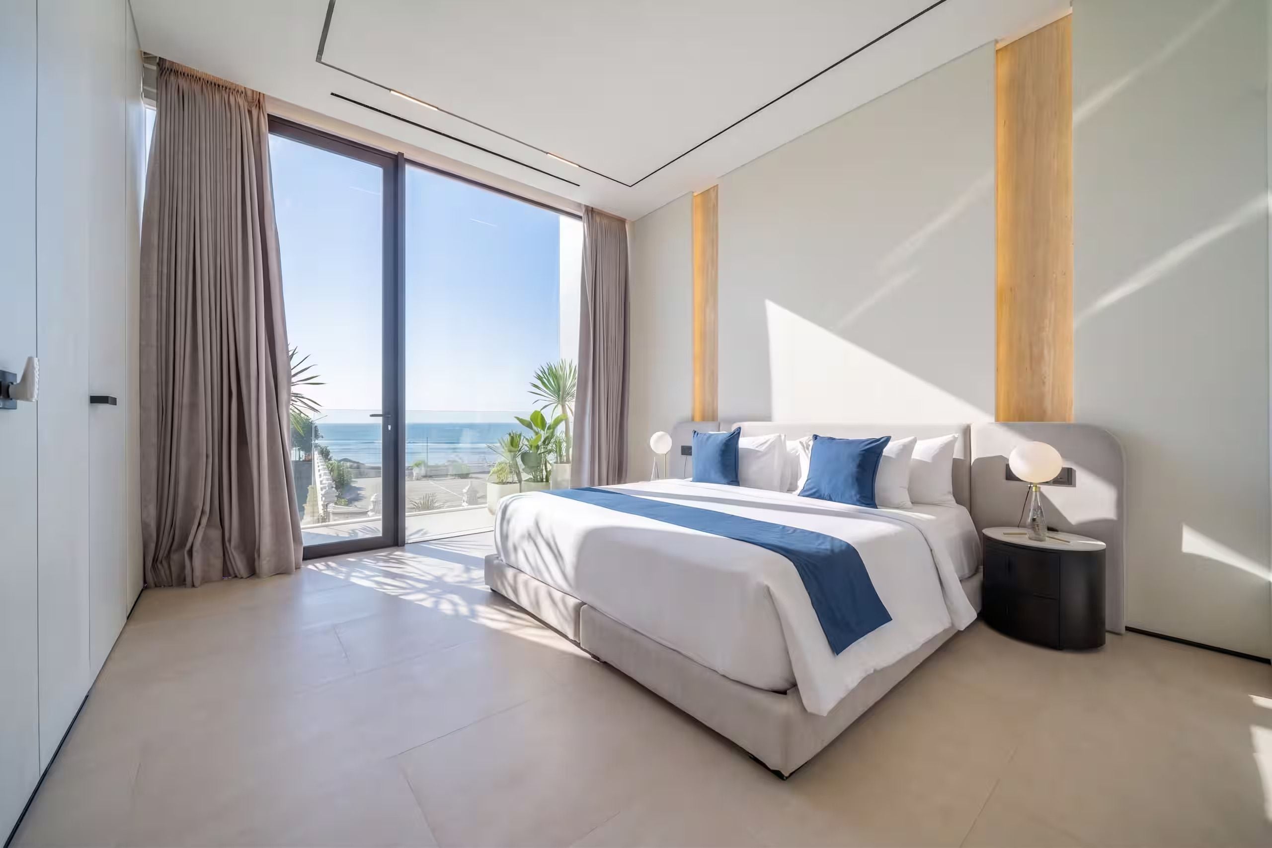 Habitación de hotel moderna con una cama grande, una mesita de noche y vista al océano.