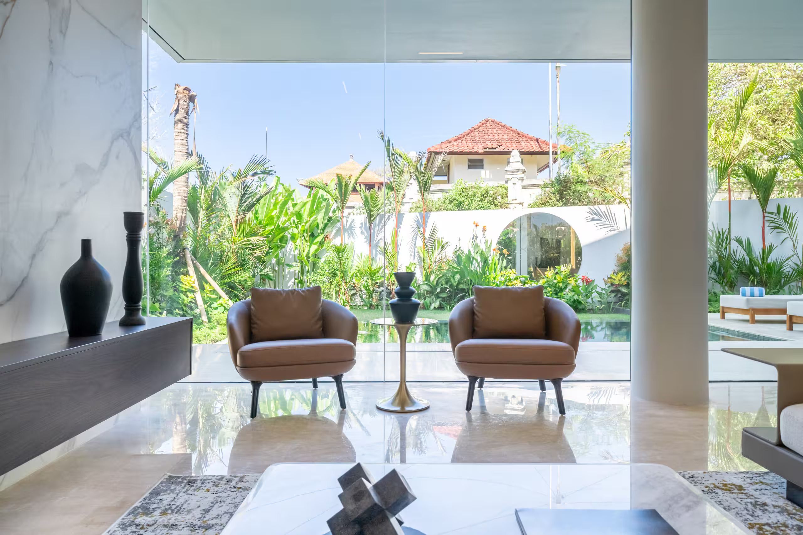 A modern living room with two leather sofas, a glass coffee table, and a view of a pool and garden.