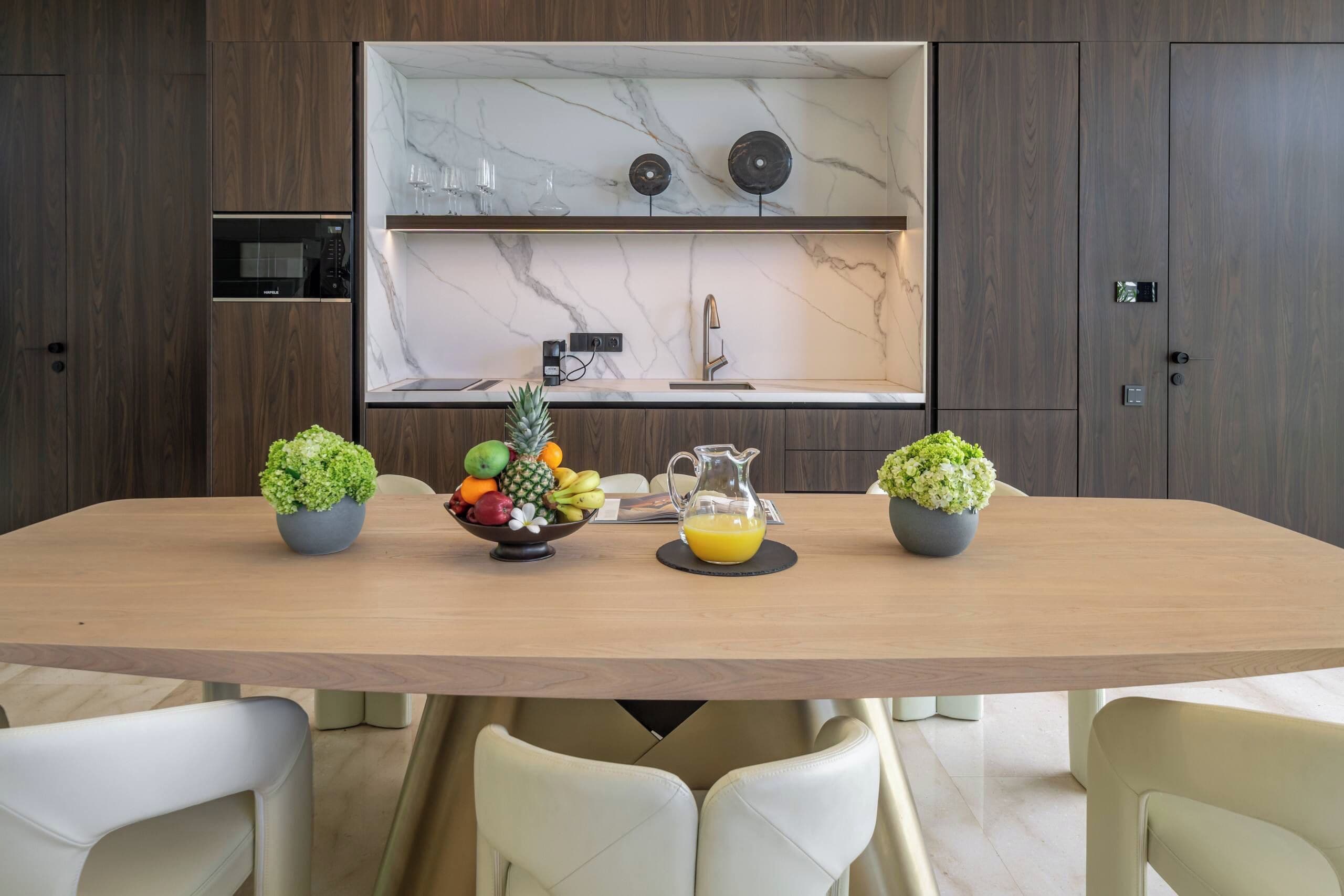 Een moderne keuken met een marmeren achterwand, houten kastjes en een eettafel met stoelen.