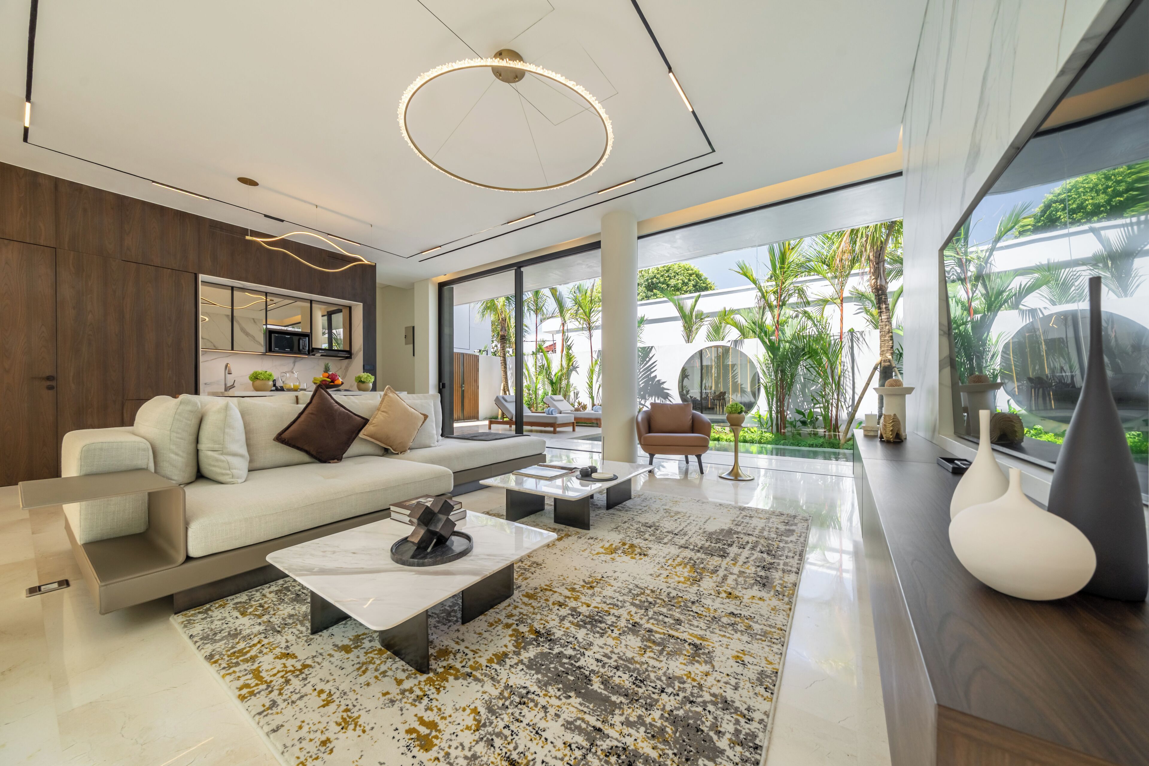 A modern living room with a sofa, coffee table, and a view of a tropical garden through large windows.