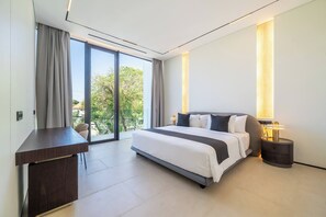 A modern hotel room with a large bed, a desk, and a view of greenery outside. - Nusa Dua Ocean View Luxury Villas (Kuta Selatan)