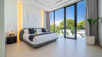 A modern bedroom with a large bed, a bedside table with a lamp, a wall art piece, and a view of greenery through large windows.