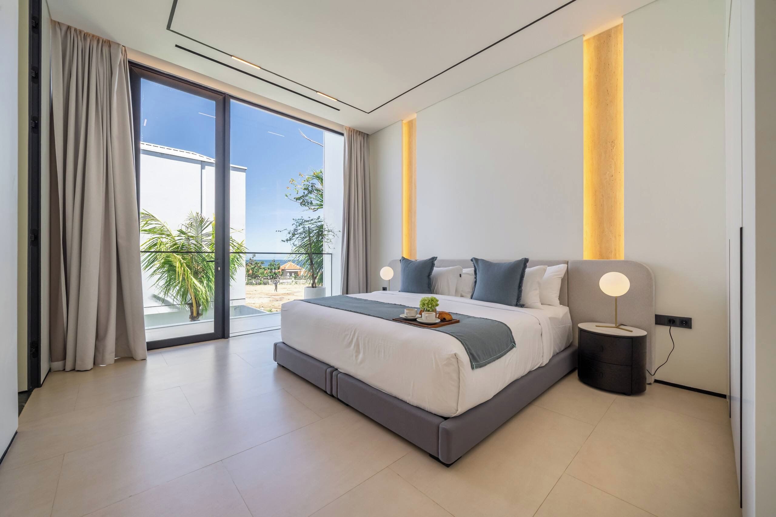 Un dormitorio moderno con una cama grande, una mesita de noche con lámpara y vistas al exterior.