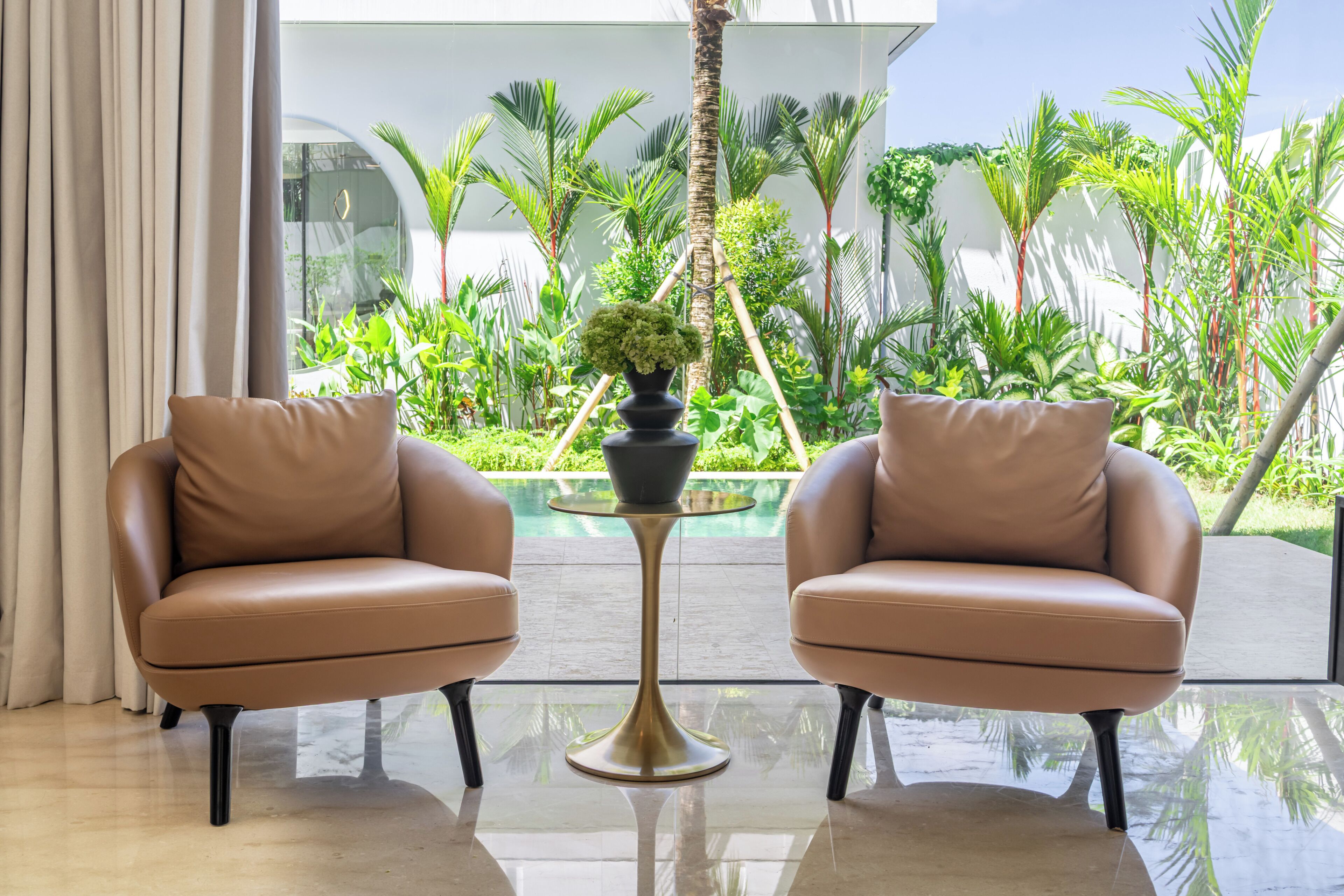 A modern interior with two leather armchairs facing a glass table with a potted plant.