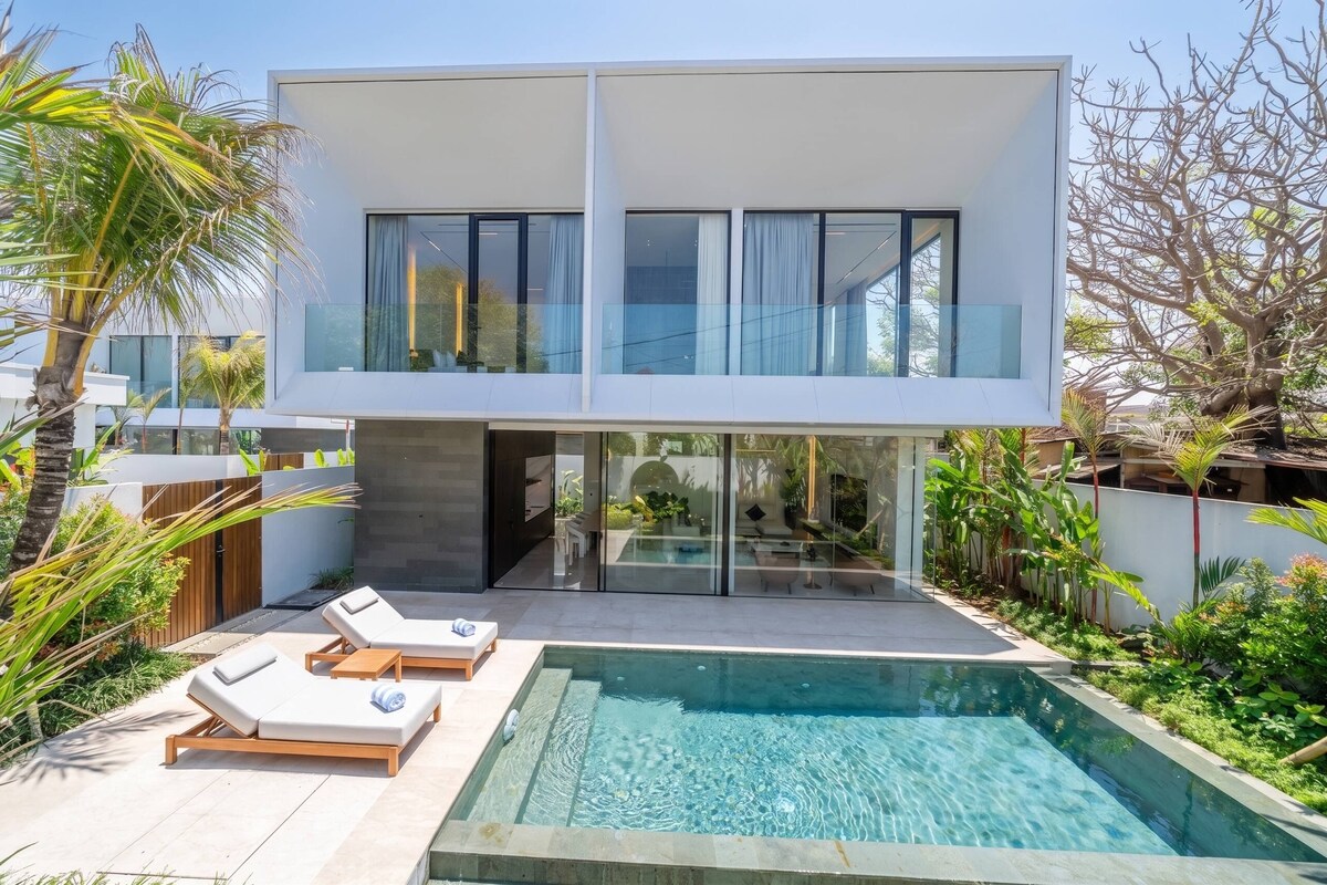 A modern two-story house with a swimming pool, lounge chairs, and a garden.