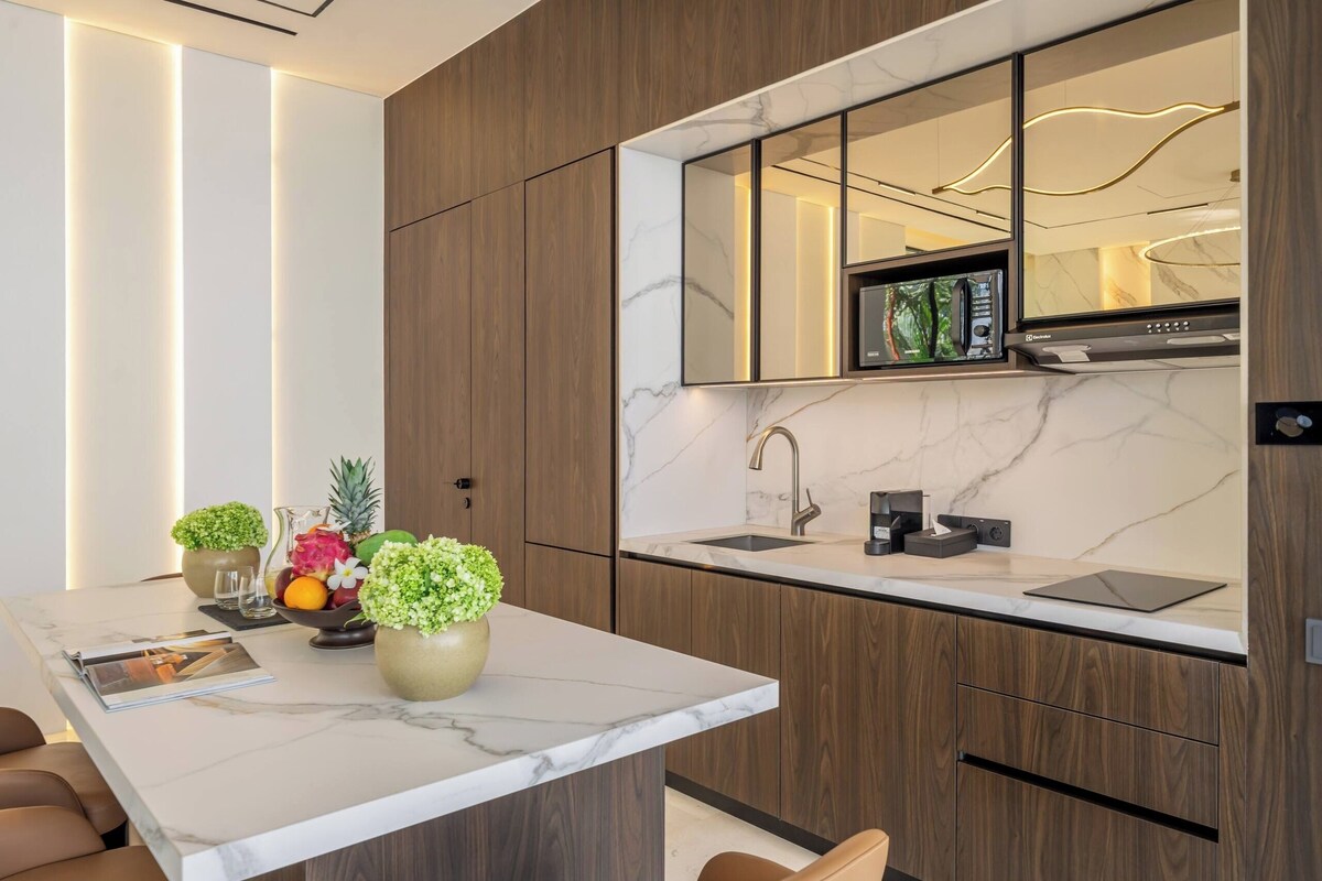A modern kitchen with a marble countertop, wooden cabinets, a built-in microwave, and a sleek faucet.
