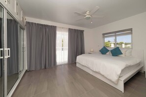 Une chambre à coucher avec un lit, un ventilateur de plafond, une fenêtre avec des rideaux et une porte-fenêtre coulissante.