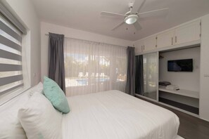 Ein Schlafzimmer mit einem Bett, einem Deckenventilator, einem Fernseher auf einem Schrank und Blick auf einen Pool.