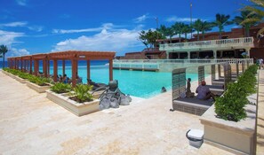 Ein Poolbereich eines Resorts mit freiem Blick auf den Ozean, einem überdachten Sitzbereich und einer Brücke, die verschiedene Bereiche des Anwesens verbindet.