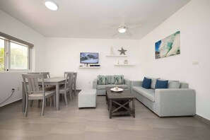 Ein modernes Wohnzimmer mit Essbereich, einem grauen Sofa, einem Couchtisch und einem Deckenventilator.