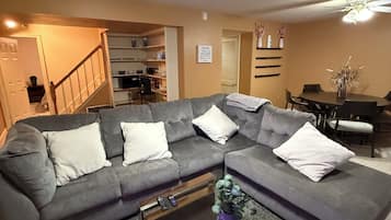 Un salon avec un canapé d’angle, une table basse, un ventilateur de plafond et, au fond, un coin repas.
