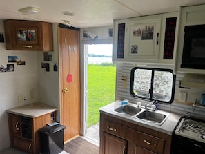 A compact kitchen with a sink, stove, and a window overlooking a grassy area. - Missouri River Cabin near Northwest Missouri, Southeast Nebraska, Southwest Iowa (Hamburg)