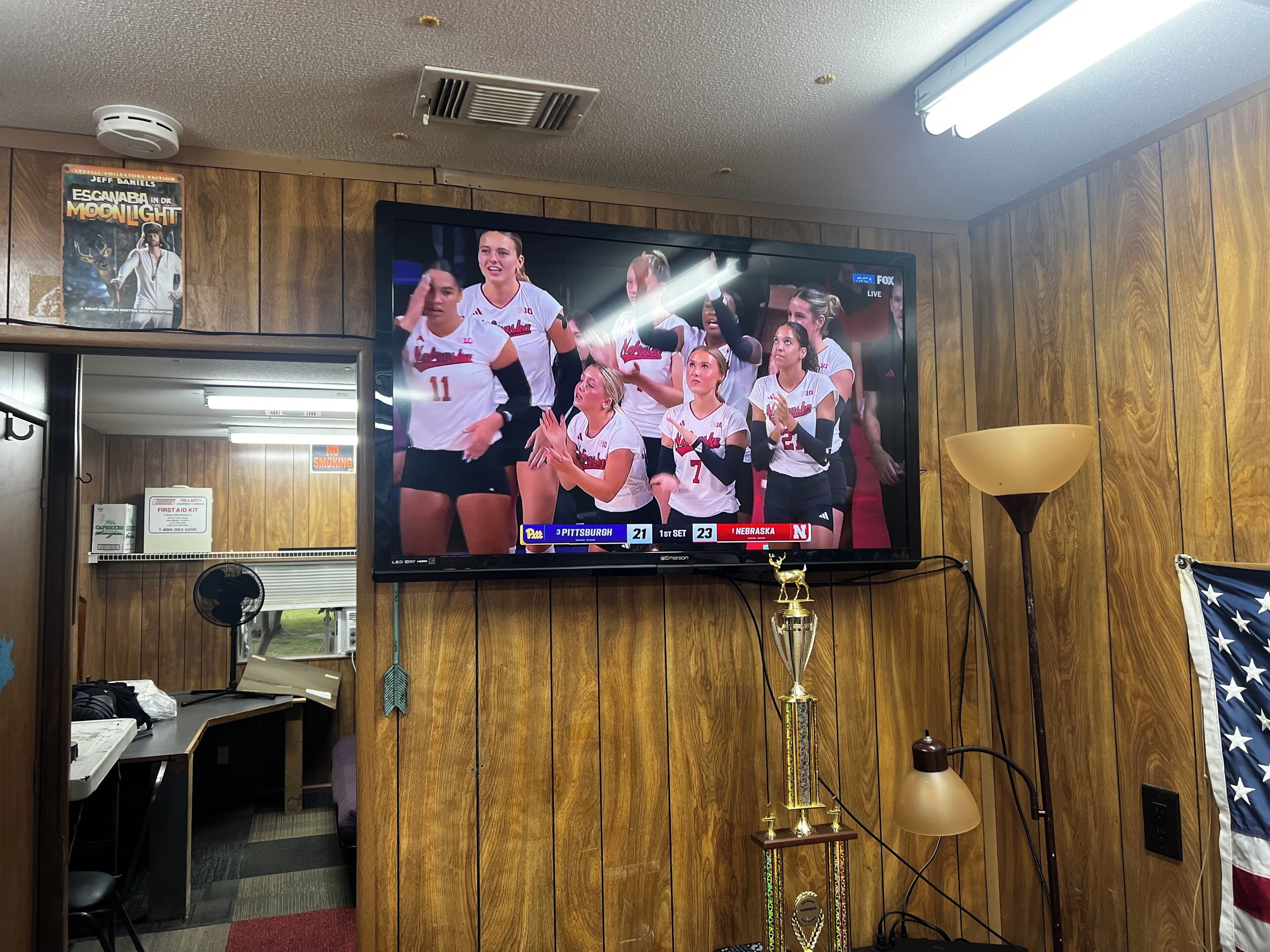 A room with a television displaying a sports event, a trophy, and wooden paneling.