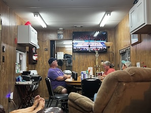A room with wooden paneling, a television mounted on the wall, and a table with various items.