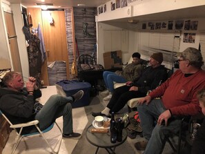 A group of people seated in a room with a wooden door, a stroller, and a table with bottles and a cake.