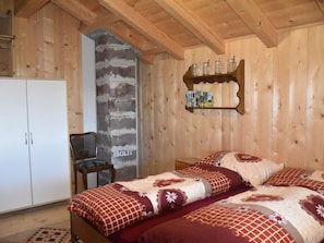 A wooden room with a bed, a chair, a wardrobe, and a shelf with books. - Alphütte Weissenberg Hütte, WC, 2 Schlafräume 5-Bettwohnung by Interhome (Lenk)