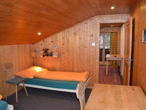 Ein kleines Zimmer mit Holzboden, einem Einzelbett, einem Tisch und einem Stuhl.
