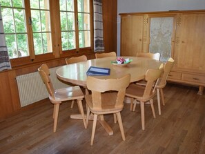 Ein Esszimmer mit einem runden Tisch, sechs Holzstühlen, einer Kommode und einem Fenster mit Vorhängen.