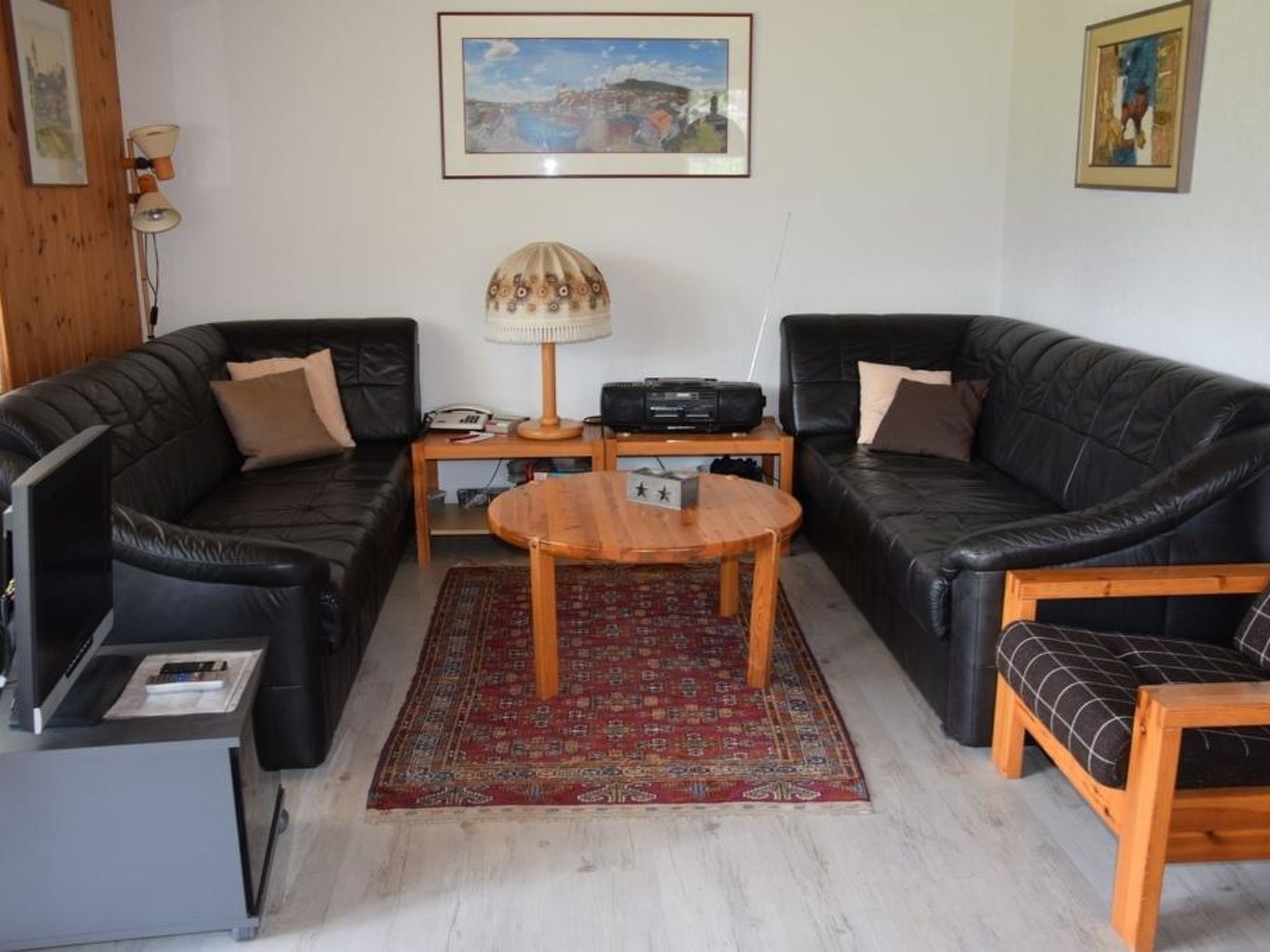A living room with two black leather sofas, a wooden coffee table, a red patterned rug, a lamp, and a framed picture on the wall.