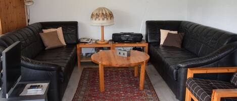 A living room with two black leather sofas, a wooden coffee table, a red patterned rug, a lamp, and a framed picture on the wall.