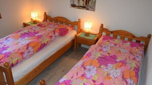 Une chambre avec deux lits en bois, chacun recouvert d’une couvre-lit à motifs floraux et agrémenté d’une table de chevet avec une lampe.
