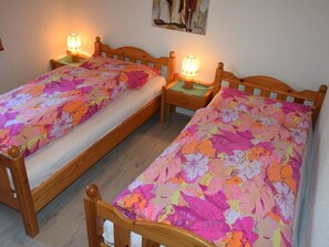 A room with two wooden beds, each with a floral bedspread and a bedside table with a lamp. - Steinbock # 2 Appartement/Fewo, Dusche oder Bad, WC, 1 Schlafraum 4-Bett-Wohnung by Interhome (Lenk)