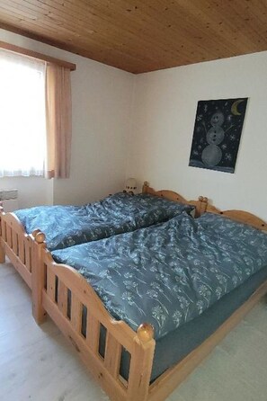 A room with a wooden bed, a window with curtains, and a wall with a night sky painting. - Steinbock # 2 Appartement/Fewo, Dusche oder Bad, WC, 1 Schlafraum 4-Bett-Wohnung by Interhome (Lenk)