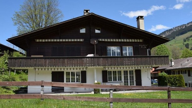 Un chalet à deux étages doté d’un balcon, de grandes fenêtres et d’une clôture en bois au premier plan.