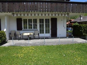 A building with a covered patio, a table, and two chairs. - Steinbock # 2 Appartement/Fewo, Dusche oder Bad, WC, 1 Schlafraum 4-Bett-Wohnung by Interhome (Lenk)