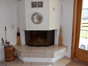 A corner fireplace with a tiled surround, a wooden bucket with tools, and a broom leaning against the wall. - Steinbock # 2 Appartement/Fewo, Dusche oder Bad, WC, 1 Schlafraum 4-Bett-Wohnung by Interhome (Lenk)
