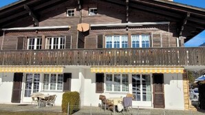 Un bâtiment en bois à deux étages, doté d’un balcon, de grandes fenêtres et d’un espace extérieur aménagé pour s’asseoir.