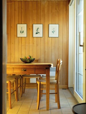 Ein Holzespeisetisch mit Stühlen, eine Fruchtschale und gerahmte Pflanzenabzüge an der Wand.