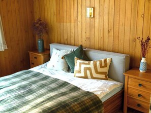 Ein Zimmer mit einem Bett, einem Nachttisch, einer Vase mit getrockneten Blumen und einer Wandleuchte.