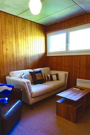 A room with a wooden paneled wall, a beige sofa with patterned cushions, a wooden coffee table, and a window with blinds. - Bergdohle Appartement/Fewo, Bad, WC, 4 oder mehr Schlafräume 7 Bett-Wohnung by Interhome (Lenk)