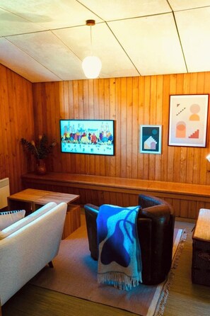 A room with wooden panel walls, a flat-screen TV mounted on the wall, a sofa, a chair, and a small table. - Bergdohle Appartement/Fewo, Bad, WC, 4 oder mehr Schlafräume 7 Bett-Wohnung by Interhome (Lenk)