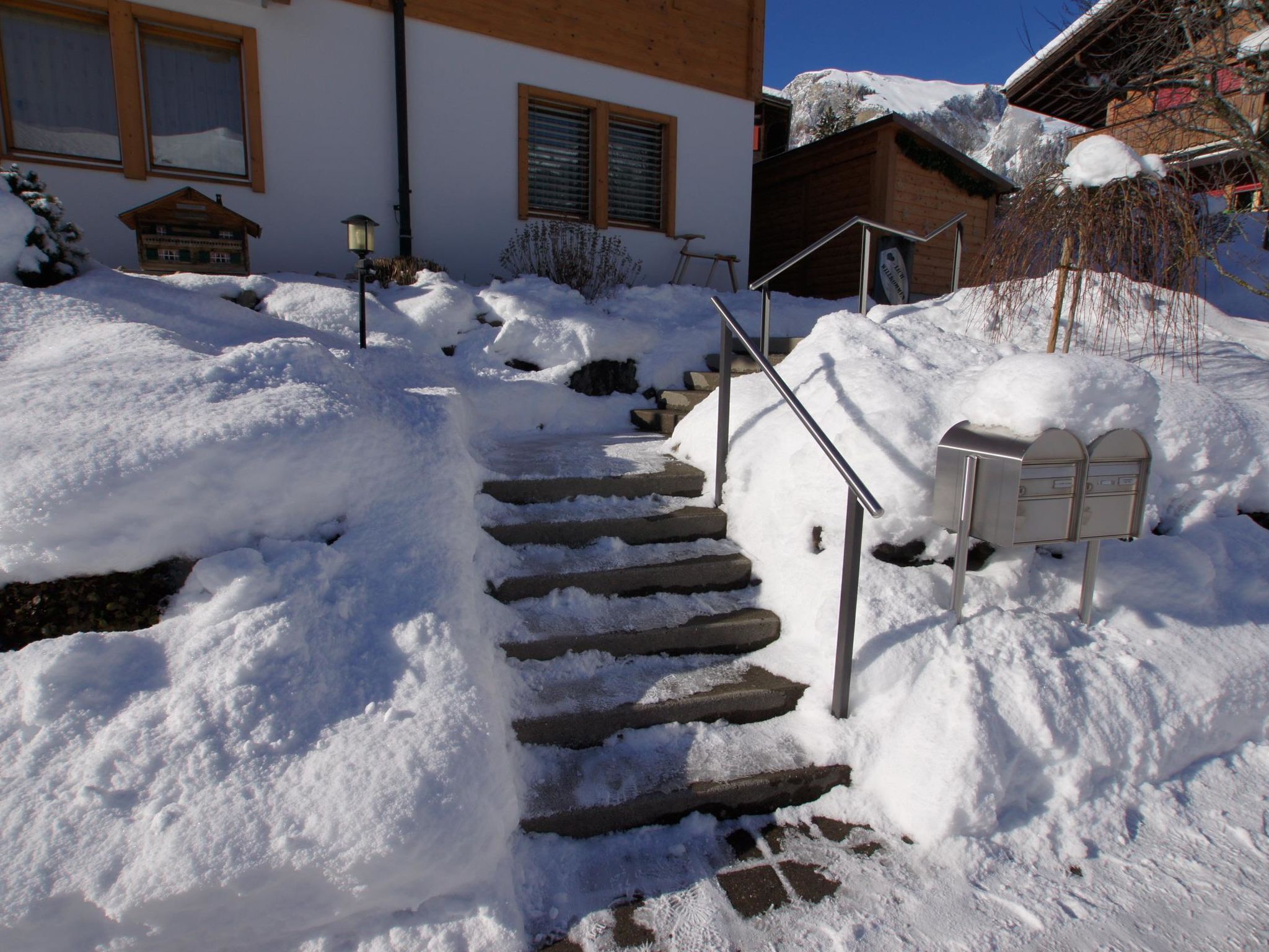 Eine schneebedeckte Treppe führt zu einem Gebäude mit einem Briefkasten und einer Laterne.