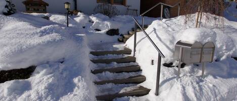 Eine schneebedeckte Treppe führt zu einem Gebäude mit einem Briefkasten und einer Laterne.