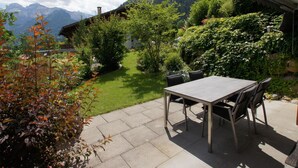 An outdoor patio with a table and chairs, surrounded by a well-maintained garden and a view of mountains. - Sina Appartement/Fewo, Dusche oder Bad, WC, 1 Schlafraum 2-Bett-Wohnung by Interhome (Lenk)