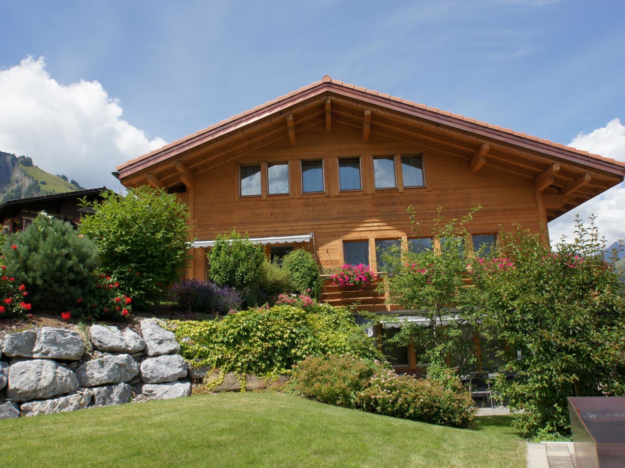 A wooden chalet with a sloped roof, multiple windows, and a well-maintained garden with various plants and flowers.