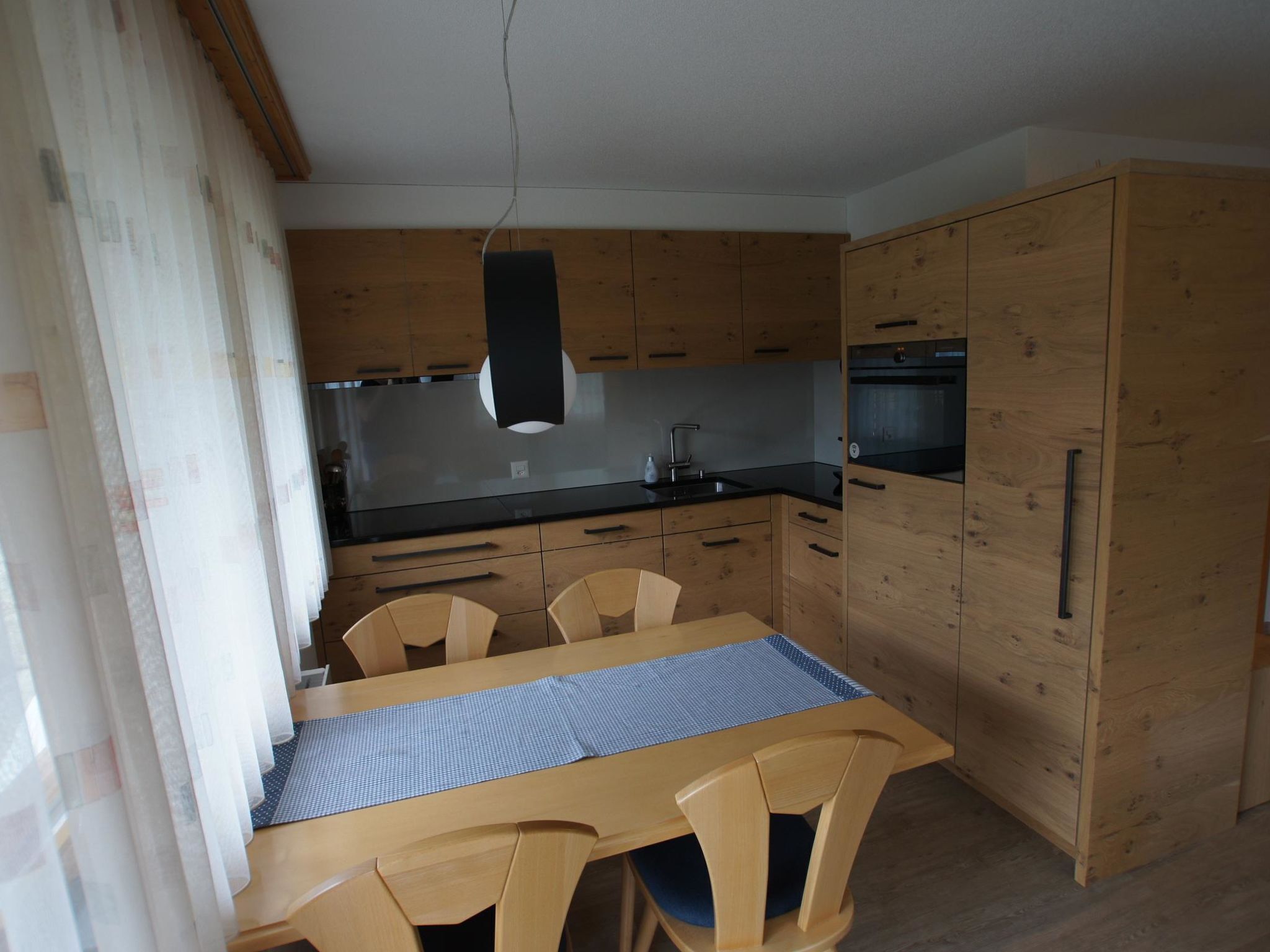 Eine kleine Küche mit Holzschränken, einer schwarzen Arbeitsplatte und einem Esstisch mit Stühlen.