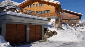 A wooden chalet with a balcony, a garage, and a mountain backdrop. - Sina Appartement/Fewo, Dusche oder Bad, WC, 1 Schlafraum 2-Bett-Wohnung by Interhome (Lenk)