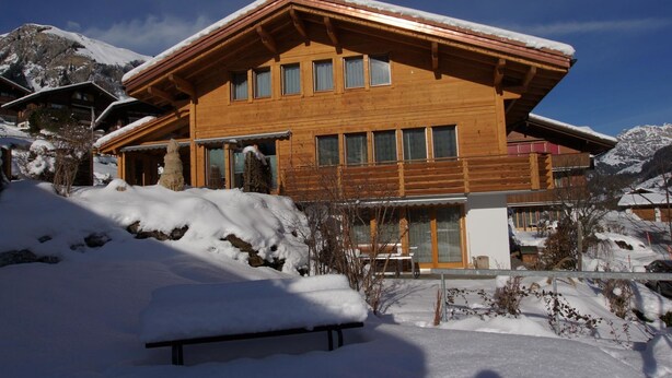 A wooden chalet with multiple windows and a balcony, surrounded by snow-covered mountains. - Sina Appartement/Fewo, Dusche oder Bad, WC, 1 Schlafraum 2-Bett-Wohnung by Interhome (Lenk)
