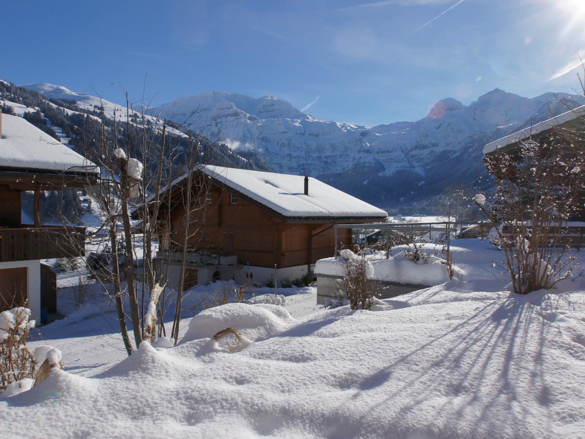 Una xalet de fusta amb el teulat cobert de neu, envoltada per terreny i muntanyes nevades al fons.