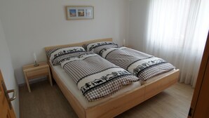 A bedroom with a wooden bed, a nightstand, a bedside table, and a picture on the wall. - Sina Appartement/Fewo, Dusche oder Bad, WC, 1 Schlafraum 2-Bett-Wohnung by Interhome (Lenk)