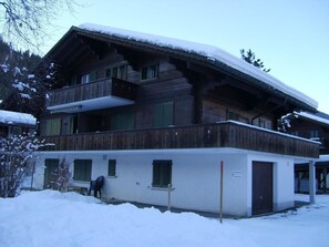 Un chalet en bois à deux étages, doté d’un balcon et entouré de neige.