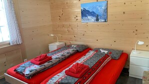 A wooden cabin room with a bed, two bedside tables, a window with curtains, and a painting on the wall. - Elena # 2 Appartement/Fewo, Dusche oder Bad, WC, 1 Schlafraum 2-Bett-Wohnung by Interhome (Lenk)
