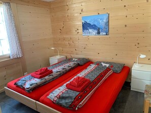 Ein Zimmer in einer Holzhütte mit einem Bett, zwei Nachttischen, einem fenster mit Vorhängen und einem Bild an der Wand.